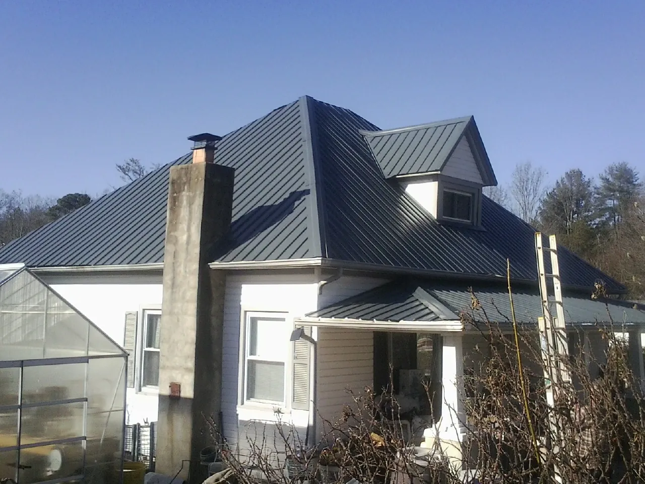 Dark blue standing seam metal roof on a white farmhouse with dormer — Slate & Tile Roof Repair by Roofing Brothers in Luthersville