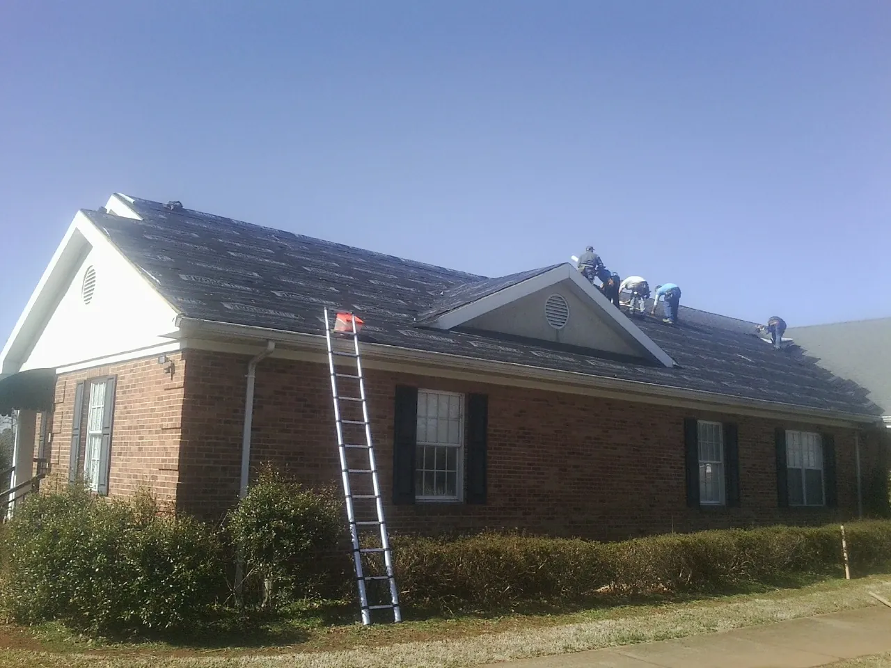 Crew tearing shingles off a brick ranch roof with a ladder set — Metal Roof Repair work by our crew in Luthersville