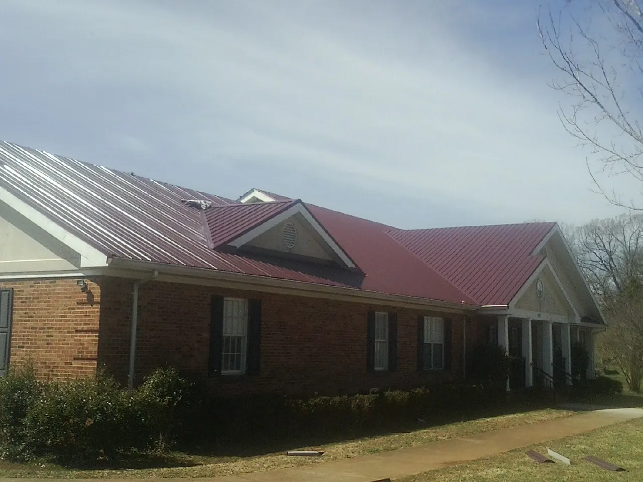 Red metal roof with gabled entries on a long brick building, from a Hail Damage Roof Repair job in Luthersville