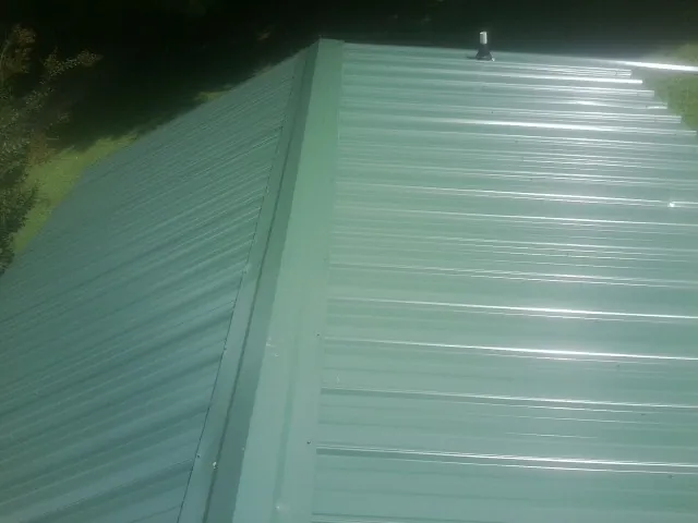 New green metal panels meeting at the ridge of a roof — Flat Roof Repair work by our crew in Luthersville