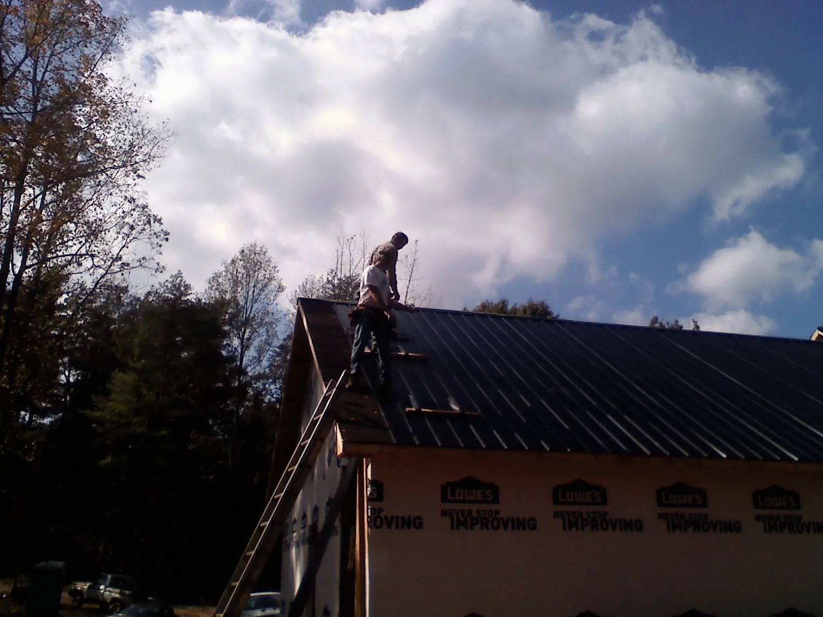 Roofer fastening dark metal panels high against a cloudy sky, from a Roof Inspection job in Luthersville
