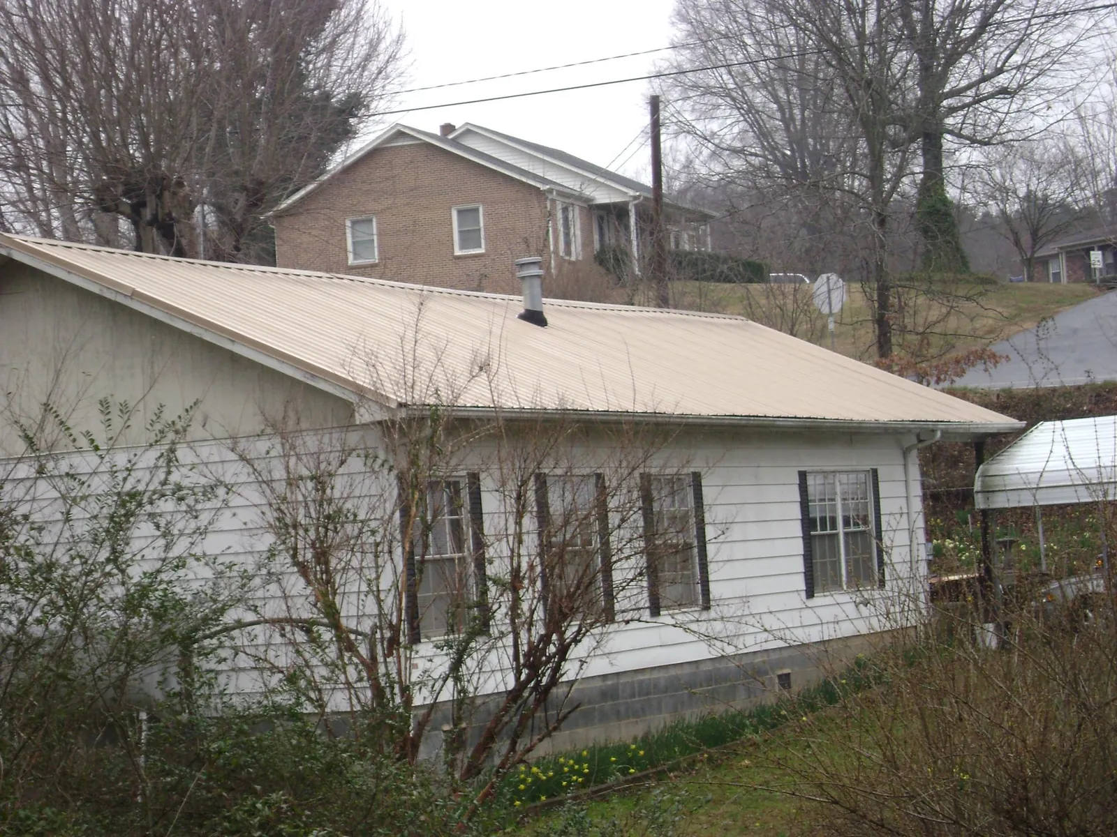 Tan metal roof on a white sided house set into a hillside — Commercial Roofing by Roofing Brothers in Luthersville